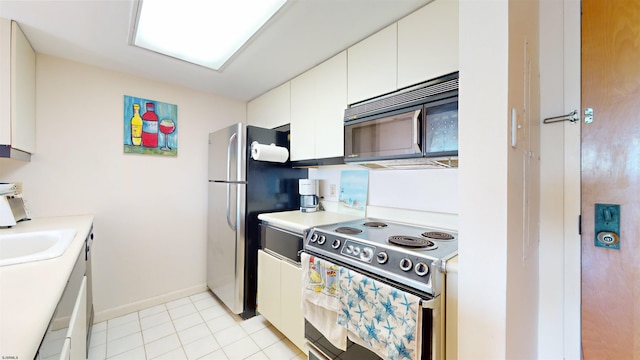 kitchen with stainless steel fridge, electric range oven, sink, white cabinets, and light tile patterned flooring