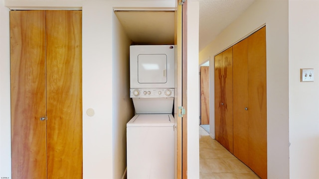 laundry room with stacked washing maching and dryer, a textured ceiling, and light tile patterned floors