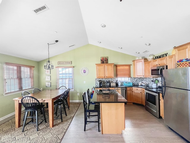 kitchen with light wood-type flooring, stainless steel appliances, vaulted ceiling, decorative light fixtures, and a center island