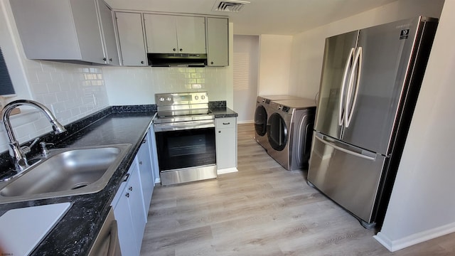 kitchen featuring backsplash, sink, light hardwood / wood-style flooring, appliances with stainless steel finishes, and washing machine and clothes dryer