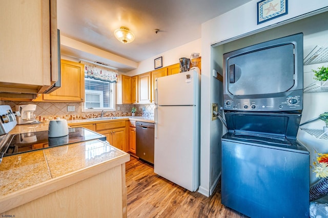 kitchen featuring sink, stacked washer and dryer, decorative backsplash, light hardwood / wood-style floors, and stainless steel appliances