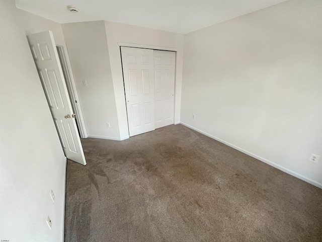 unfurnished bedroom with dark carpet and a closet