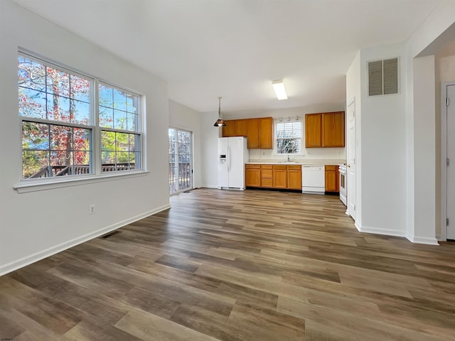 kitchen with hanging light fixtures, dark wood-type flooring, white appliances, and sink