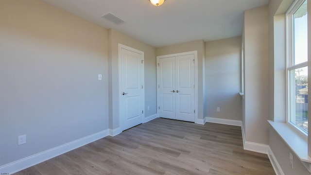 unfurnished bedroom with a closet, light hardwood / wood-style floors, and multiple windows