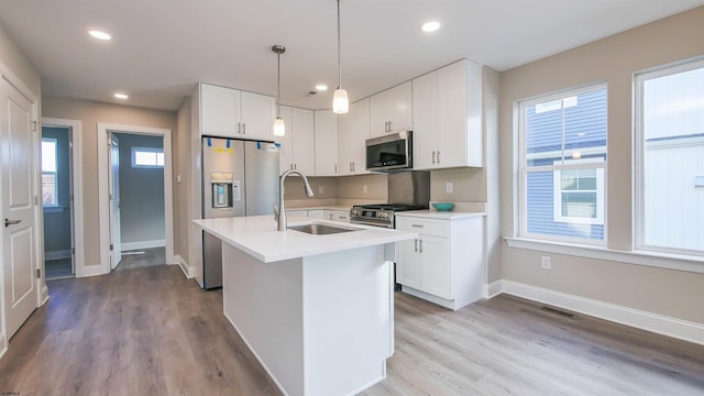 kitchen with a kitchen island with sink, white cabinets, sink, hanging light fixtures, and stainless steel appliances