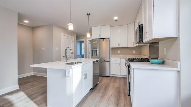 kitchen featuring appliances with stainless steel finishes, sink, decorative light fixtures, white cabinets, and an island with sink