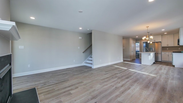 unfurnished living room featuring light hardwood / wood-style floors, sink, and an inviting chandelier