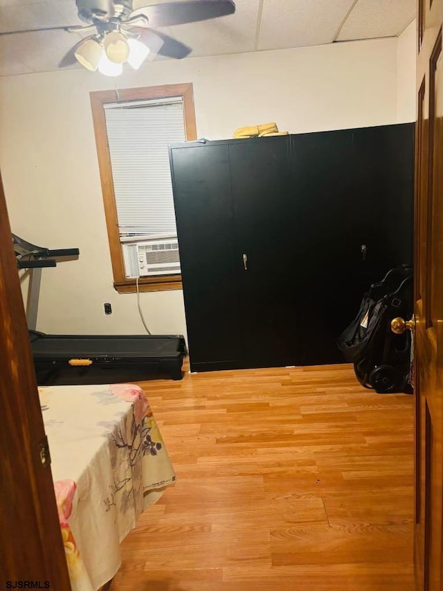 bedroom featuring hardwood / wood-style floors, ceiling fan, cooling unit, and a drop ceiling