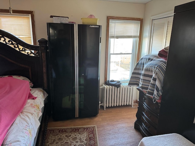 bedroom with a closet, light hardwood / wood-style flooring, black fridge, and radiator