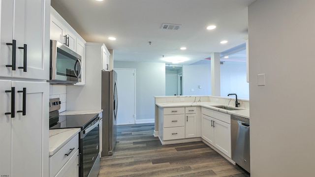 kitchen with kitchen peninsula, stainless steel appliances, dark wood-type flooring, sink, and white cabinets