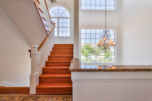 stairs featuring hardwood / wood-style flooring, a towering ceiling, and a chandelier