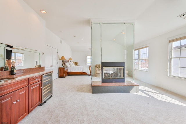 living room with sink, wine cooler, vaulted ceiling, a tiled fireplace, and light carpet