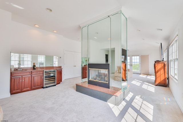 carpeted living room featuring a multi sided fireplace, sink, and beverage cooler