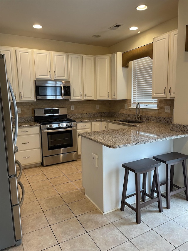 kitchen with white cabinets, sink, light tile patterned floors, appliances with stainless steel finishes, and kitchen peninsula