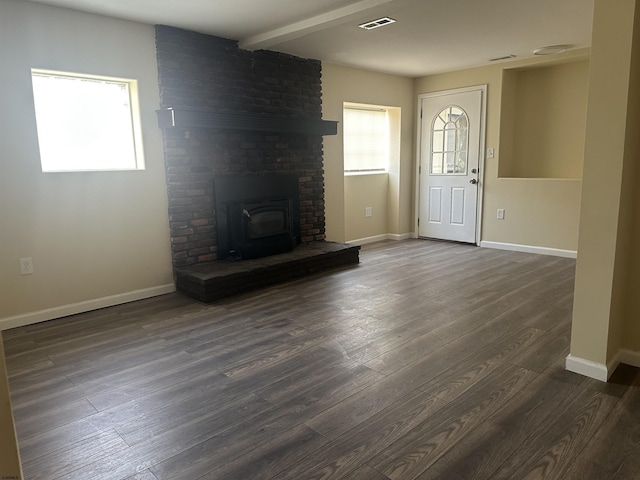 unfurnished living room featuring a wood stove, beamed ceiling, and dark wood-type flooring