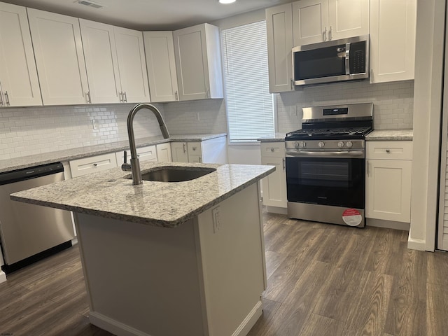 kitchen featuring a center island with sink, sink, light stone counters, white cabinetry, and stainless steel appliances