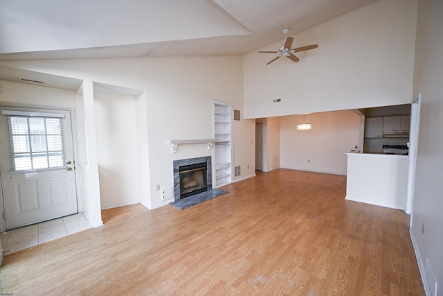 unfurnished living room featuring a high end fireplace, high vaulted ceiling, light hardwood / wood-style flooring, and ceiling fan