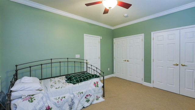 bedroom featuring ceiling fan, carpet floors, ornamental molding, and multiple closets