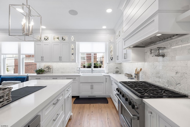 kitchen with sink, stainless steel stove, white cabinets, custom exhaust hood, and light wood-type flooring