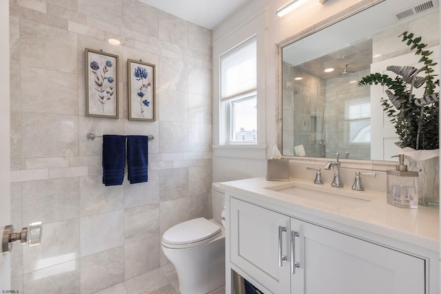 bathroom with vanity, toilet, a shower with door, and tile walls