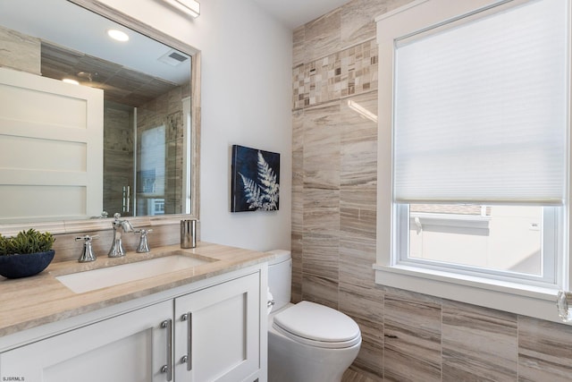 bathroom featuring vanity, tile walls, and toilet