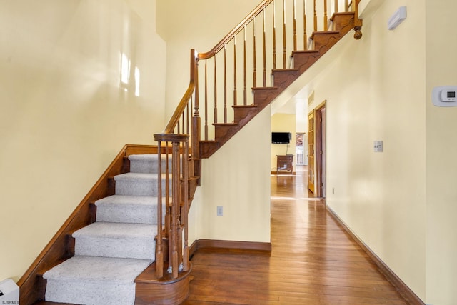 stairway featuring a towering ceiling and wood-type flooring