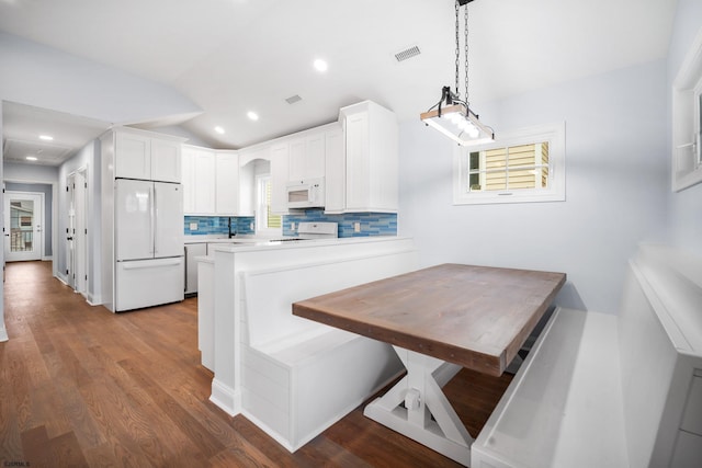 kitchen featuring vaulted ceiling, kitchen peninsula, white cabinetry, and white appliances