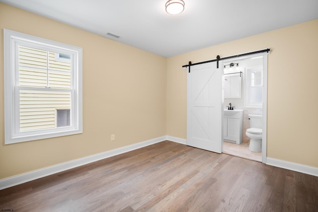 unfurnished bedroom featuring a barn door, light hardwood / wood-style floors, sink, and ensuite bath