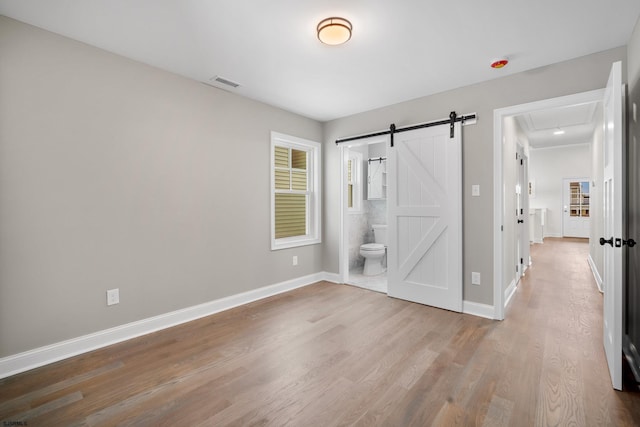 unfurnished bedroom with ensuite bath, light hardwood / wood-style floors, and a barn door