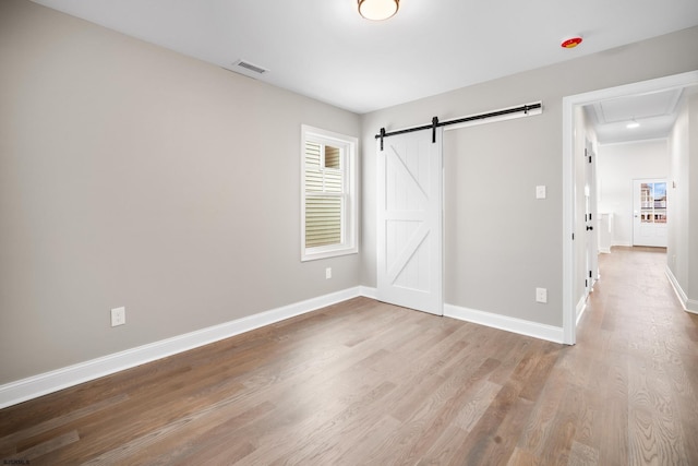 unfurnished bedroom with a barn door and light hardwood / wood-style flooring