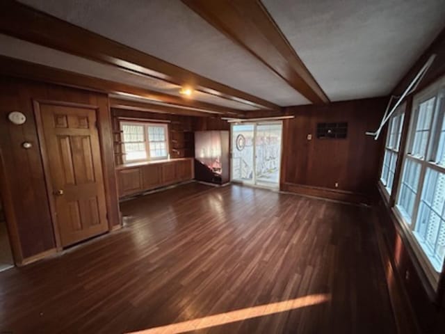 unfurnished living room featuring wood walls, beam ceiling, and dark hardwood / wood-style flooring