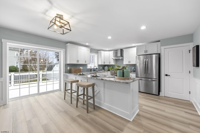 kitchen featuring white cabinetry, stainless steel fridge, light hardwood / wood-style floors, and wall chimney range hood