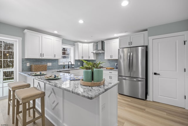 kitchen with stainless steel appliances, white cabinetry, light hardwood / wood-style floors, and wall chimney range hood