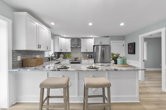 kitchen featuring white cabinets, wall chimney exhaust hood, light wood-type flooring, and appliances with stainless steel finishes