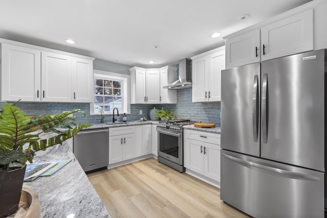 kitchen with sink, wall chimney exhaust hood, stainless steel appliances, light stone counters, and light hardwood / wood-style floors