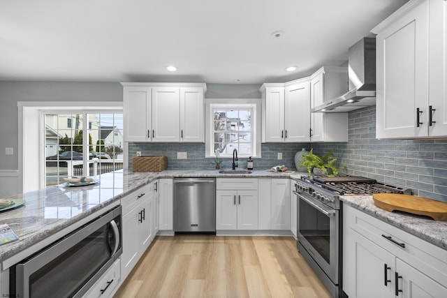 kitchen featuring wall chimney exhaust hood, stainless steel appliances, a wealth of natural light, and light hardwood / wood-style flooring