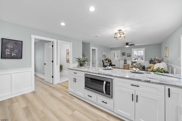 kitchen with ceiling fan, stainless steel microwave, white cabinets, and light hardwood / wood-style flooring