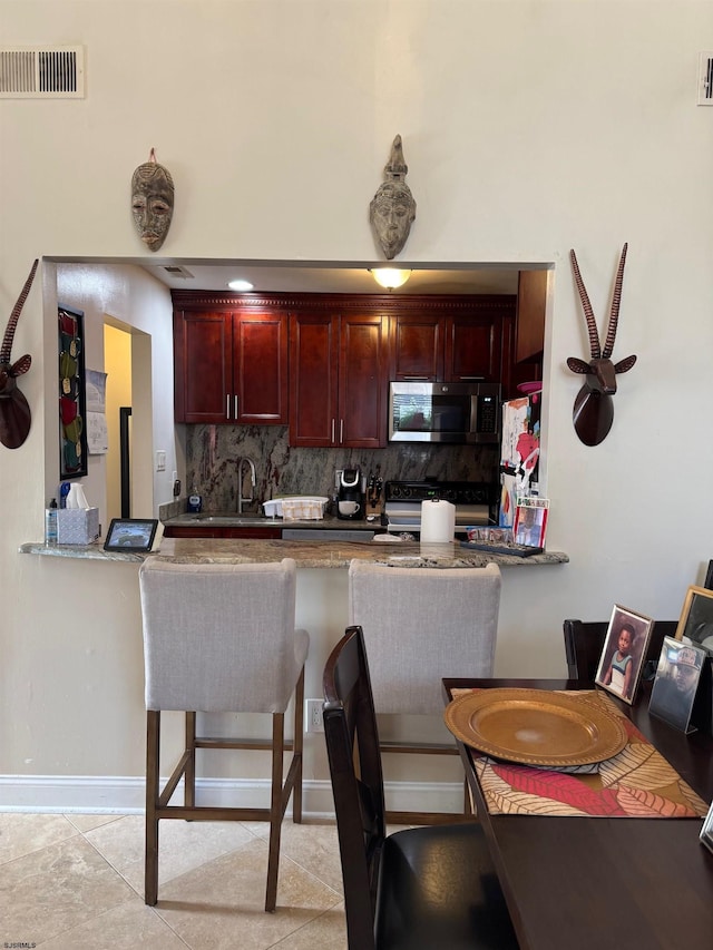 kitchen with kitchen peninsula, black stove, backsplash, and light tile patterned flooring