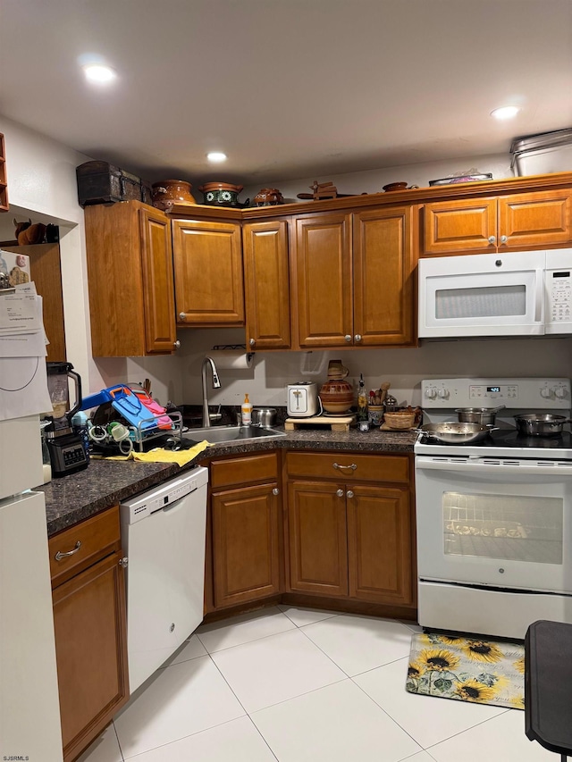 kitchen featuring dark stone countertops, white appliances, sink, and light tile patterned floors