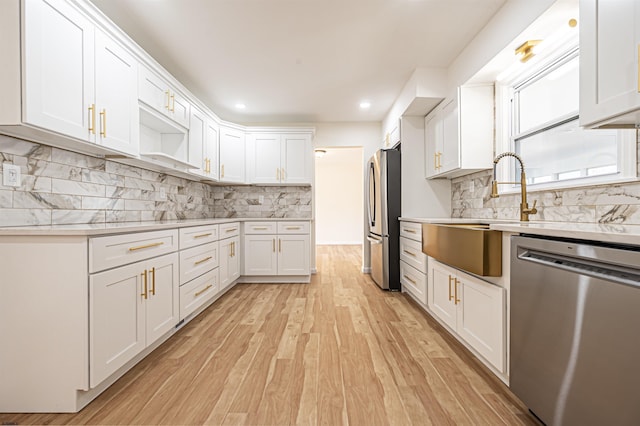 kitchen with white cabinets, tasteful backsplash, appliances with stainless steel finishes, and light hardwood / wood-style flooring