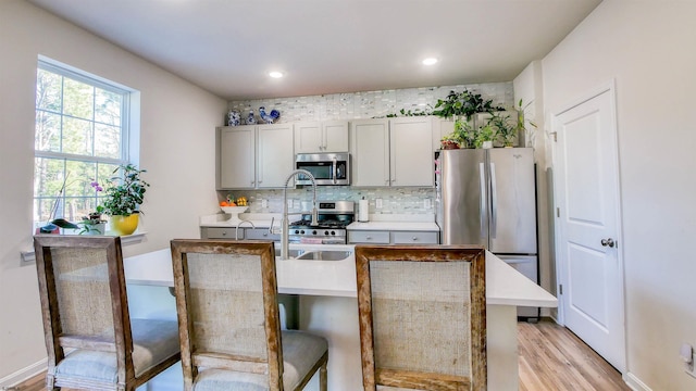 kitchen featuring a center island with sink, a kitchen breakfast bar, light hardwood / wood-style flooring, gray cabinets, and appliances with stainless steel finishes