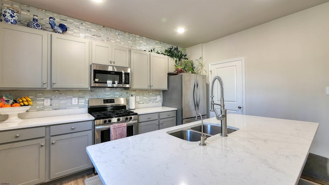 kitchen with appliances with stainless steel finishes, backsplash, light stone counters, gray cabinetry, and sink