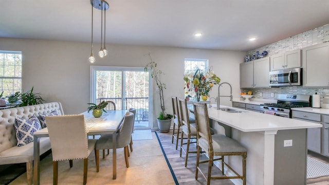 kitchen with gray cabinetry, a center island with sink, stainless steel appliances, and decorative light fixtures