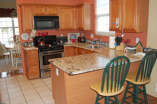 kitchen featuring kitchen peninsula, a kitchen breakfast bar, light stone countertops, stainless steel gas range oven, and sink