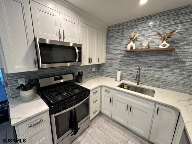 kitchen with backsplash, sink, white cabinets, and stainless steel appliances