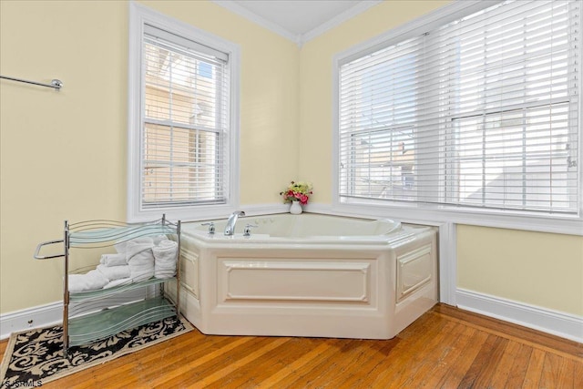 bathroom featuring hardwood / wood-style floors, ornamental molding, a tub to relax in, and a wealth of natural light