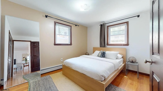 bedroom featuring light wood-type flooring, baseboard heating, and multiple windows