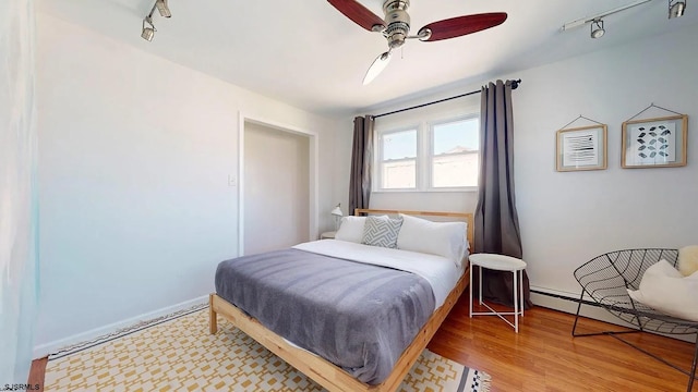 bedroom with hardwood / wood-style flooring, ceiling fan, baseboard heating, and track lighting