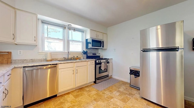 kitchen featuring white cabinets, stainless steel appliances, light stone counters, and sink