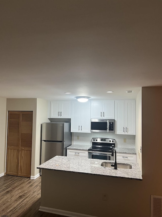 kitchen with sink, dark wood-type flooring, light stone counters, white cabinets, and appliances with stainless steel finishes